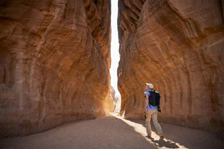 homem caminhando entre dois paredões de pedra para chegar a Petra